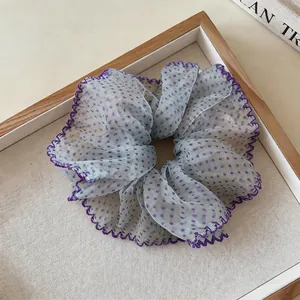 Close-up of a blue chiffon scrunchie with purple polka dots and lace edges on a wooden tray