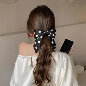 Detailed view of a French style black satin polka dot bow hair scrunchie on a ponytail