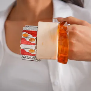 Detailed view of layered enamel metal stretch bracelet and marbled resin geometric bangles.