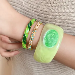 Close-up detail of three stylish green-toned enamel and resin bracelets on a model wrist.