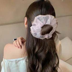 Close-up view of a pink polka dot chiffon scrunchie with gold lace trim on model