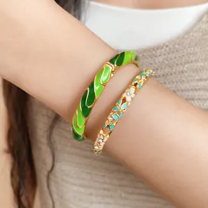 Detail shot of gold-plated enamel bangles with green patterns and floral crystals on a wrist.