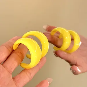 Macro view of vibrant yellow C-shaped resin hoop earrings in a reflective mirror scene