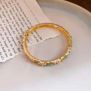 Detailed close-up of gold-plated hinged bangle with turquoise and pink enamel heart patterns