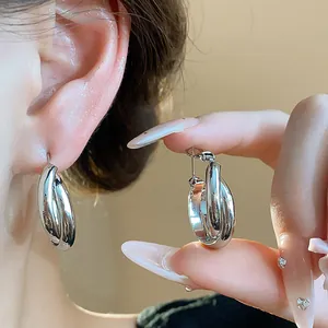 Close-up of minimalist 18K silver-plated hoop earrings shown on ear and held by hand