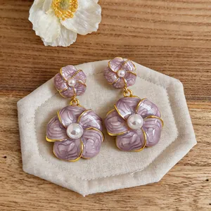 Nahaufnahme von eleganten lila Blumenohrringen mit Perlenmitte und Goldrand Details