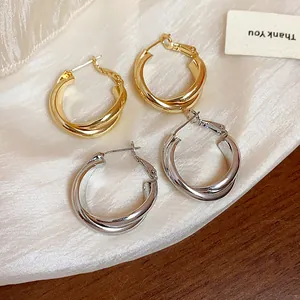 Detail view of 18K gold and silver plated intertwined hoop earrings on silk fabric.