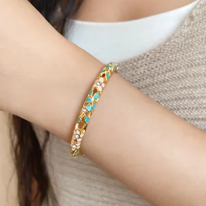 Close-up view of an elegant gold floral enamel bangle with sparkling crystals on a wrist