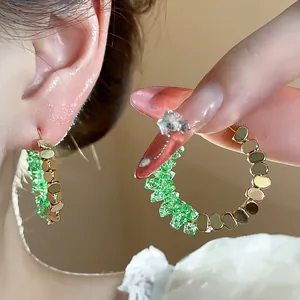 Close-up view of 14K gold plated hoop earrings with vibrant green crushed crystals.