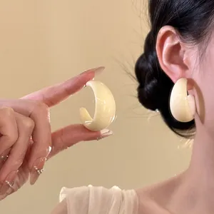 Detailed close-up of a cream-colored minimalist C-shaped resin earring worn on an ear