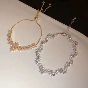 Close-up of elegant zircon wheat ear and pearl zigzag bracelets on a ceramic tray.