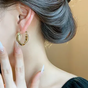Close-up detail of 18K gold-plated hoop earrings worn on ear, showcasing glossy finish