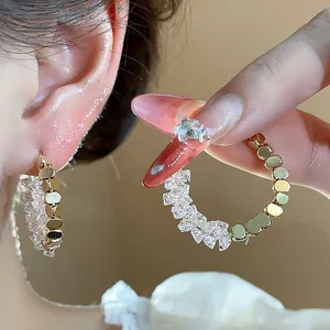 Detailed close-up of 14K gold plated crystal hoop earrings shown worn on ear and held