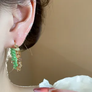 Detail view of 14K gold-plated hoop earring with sparkling green crystals on a model's ear