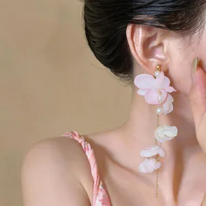 Close-up of a long floral tassel earring with pink petals and pearls worn by a model