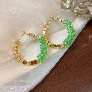 Close-up detail of 14K gold plated hoop earrings featuring vibrant green crushed crystals.