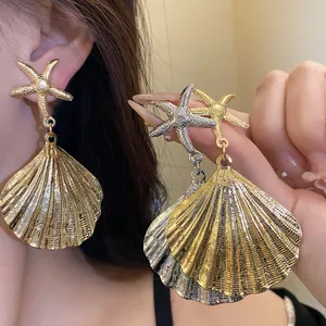 Close-up of oversized metallic pleated shell and starfish earrings with gold finish