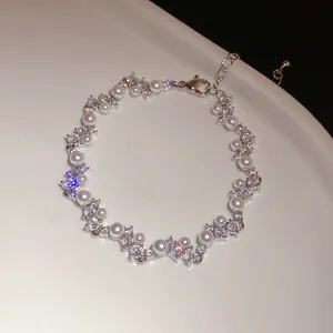 Detailed view of silver wheat-shaped bracelet with pearls and sparkling zircons.