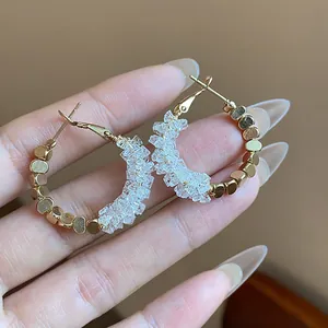 Close-up view of 14K gold plated hoop earrings with clear crystal beads held by hand