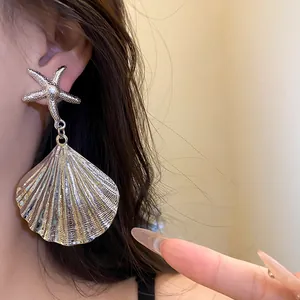 Detailed macro shot of silver starfish and pleated metal shell drop earring worn by a model