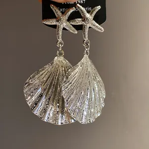 Detailed close-up of silver-tone metal starfish and pleated shell drop earrings