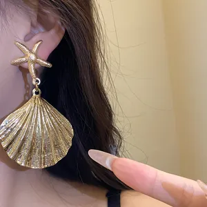 Close-up detail of gold metallic shell and starfish dangle earrings for women