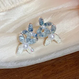 Detail view of dainty blue glass flower pearl earrings resting on elegant cream silk