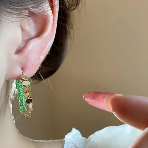 Close-up of 14K gold plated crystal hoop earring with green stones on ear.