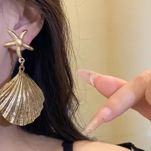 Detailed macro shot of gold-tone starfish and pleated seashell drop earrings on a model