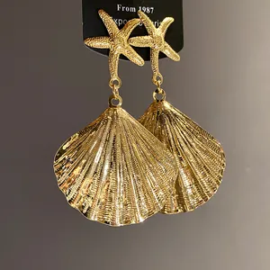 Detailed view of gold metal starfish and wrinkled shell dangle earrings with luxury texture