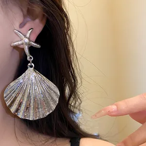 Detailed view of oversized metallic starfish and pleated shell drop earring on a model