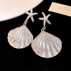 Detailed view of silver starfish and pleated shell drop earrings on a black background