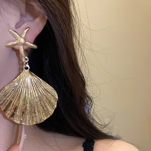 Detailed view of gold metallic seashell and starfish drop earrings worn by a model