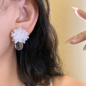 Détail d'une boucle d'oreille fleur en paillettes blanches avec une goutte d'eau transparente