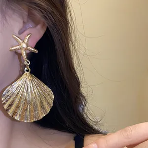Close-up of gold metal pleated shell earrings with starfish stud on model's ear