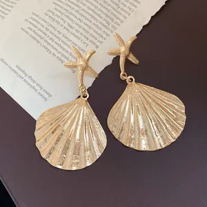 Detailed macro shot of golden metal pleated shell and starfish earrings for women