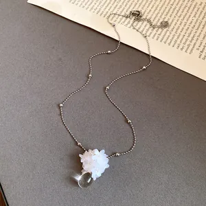 Zoom sur une fleur en paillettes blanches et un pendentif goutte d'eau sur chaîne argentée