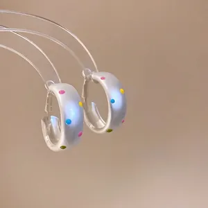 Silver brushed hoop earrings with colorful polka dots on a neutral background