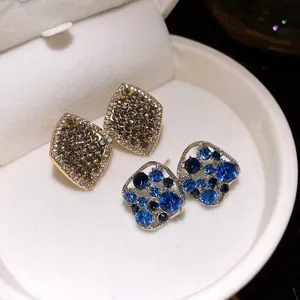 Detailansicht von Strass-Ohrsteckern in Rautenform und blau in einer weißen Schale.