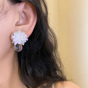 Gros plan détaillé d'une boucle d'oreille fleur à paillettes blanches avec pendentif goutte d'eau.