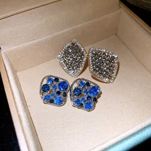 Nahaufnahme von eleganten Rauten- und quadratischen Ohrsteckern mit blauen Kristallen