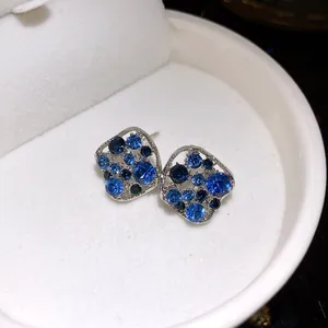Nahaufnahme silberner Rautenohrstecker mit funkelnden blauen und dunkelblauen Steinen