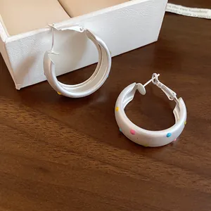 Close-up of matte silver hoop earrings featuring colorful polka dots and brushed texture