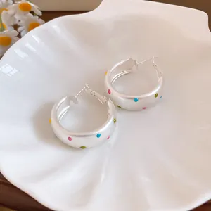 Detailed view of silver hoop earrings with colorful polka dots on a shell plate.