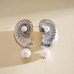 Macro detail of elegant silver seashell earrings featuring lustrous pearls for a vacation look