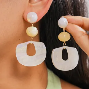 Close-up view of large pearlescent acrylic geometric drop earrings worn on model's ear