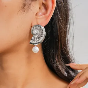 Close-up of a silver seashell earring featuring elegant white pearl details on ear.