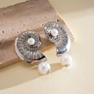 Close-up detail of silver nautical shell earrings with white pearl pendants on stone