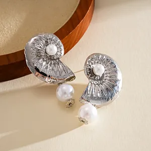 Detailed view of silver-toned nautilus earrings with pearls on a minimalist background