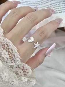 Close-up view of elegant silver seashell and starfish adjustable open ring on finger.